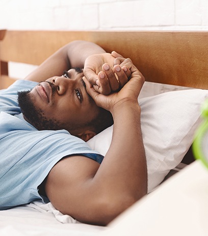 Man in blue shirt lying awake in bed