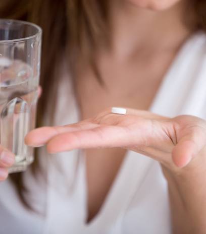 Woman holding a pill and a glass of water