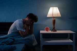 Man with sleep apnea sitting up in bed with face in hands